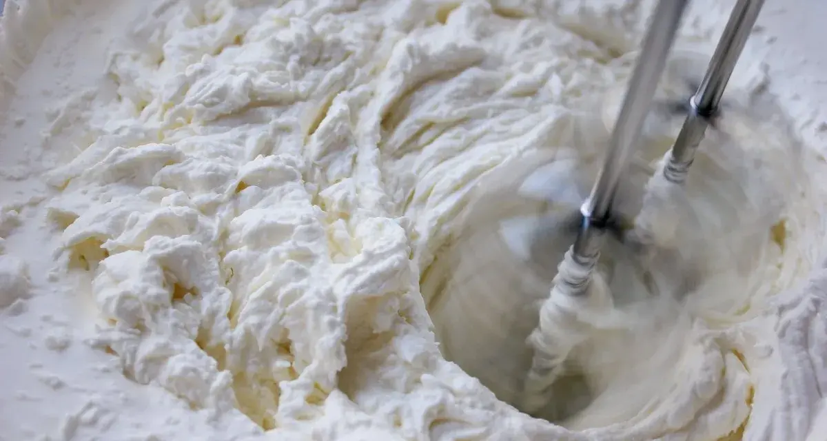 Batidora eléctrica batiendo crema blanca y espesa en un bol.