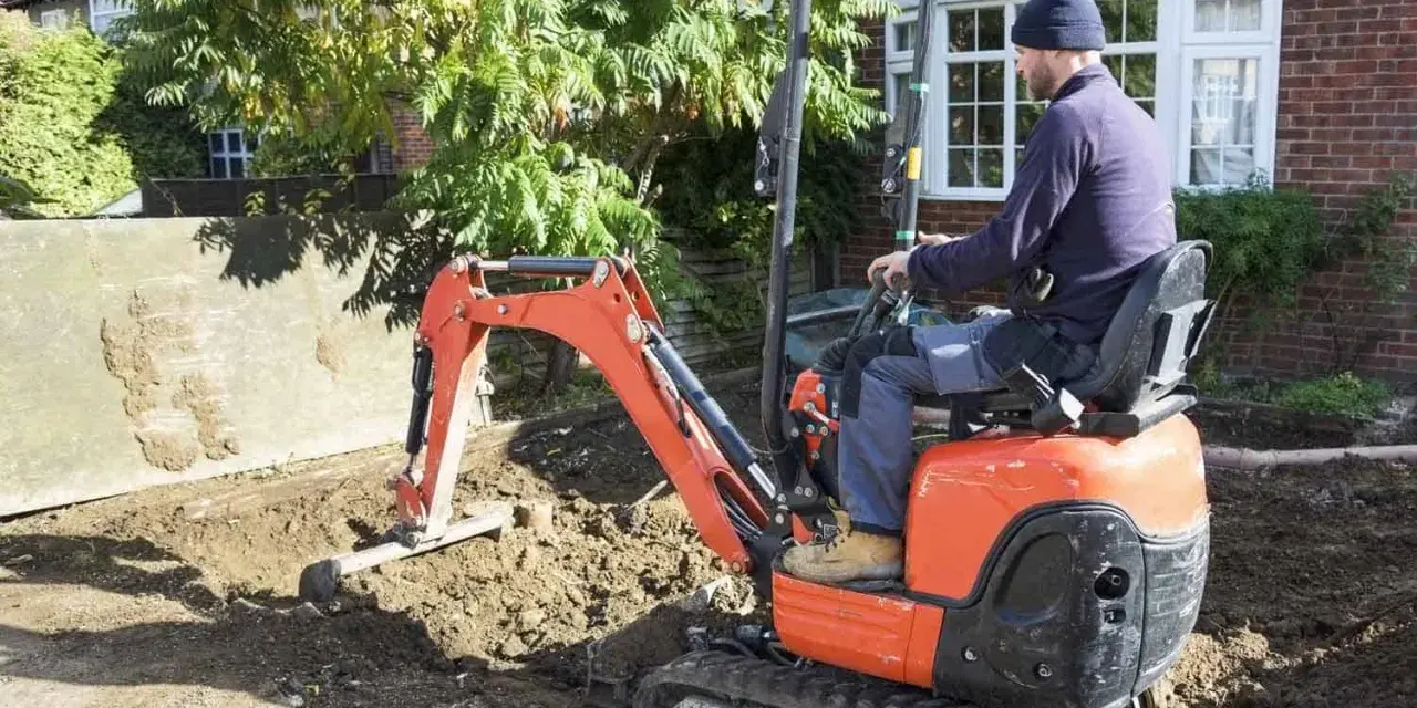 Un ouvrier manœuvre une mini-pelle orange pour des travaux de terrassement. Le prix du terrassement au m2 est une préoccupation pour ce chantier.