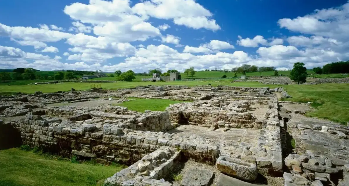 Extensive roman ruin spread across a green field under a blue sky with fluffy clouds.