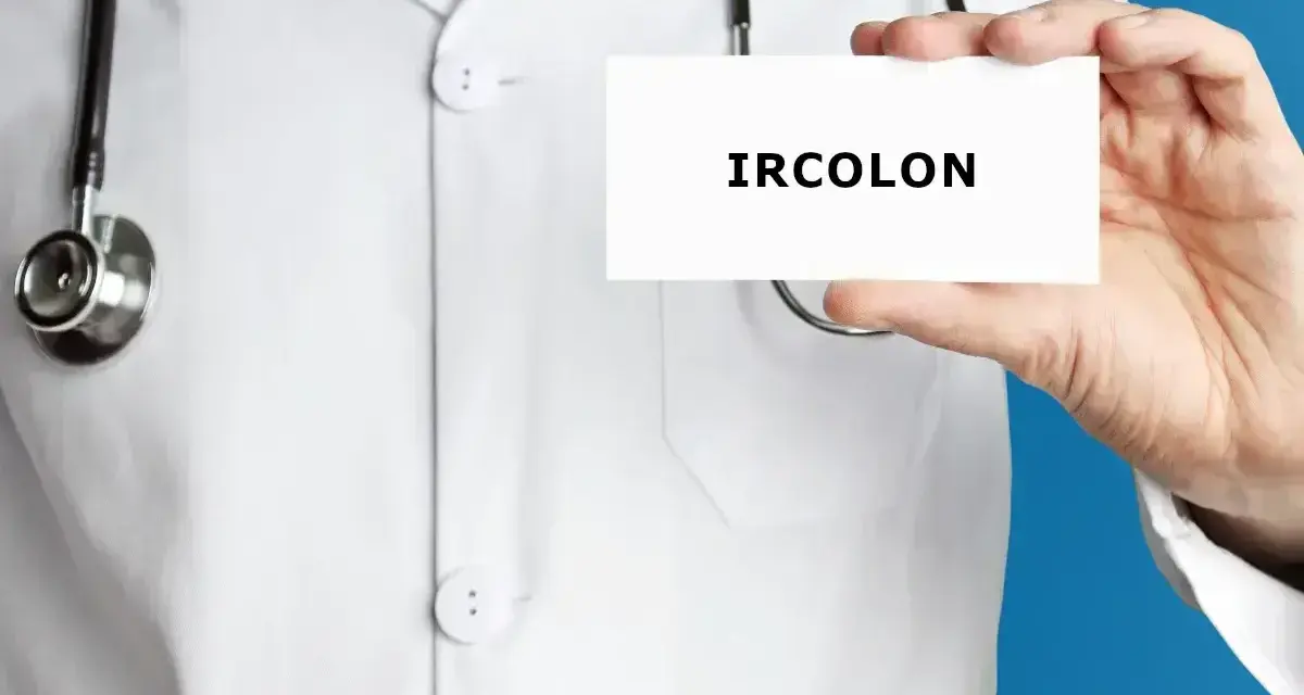 Lekarz w białym kitlu trzyma kartkę z napisem "IRCOLON". Stetoskop wisi na jego szyi.