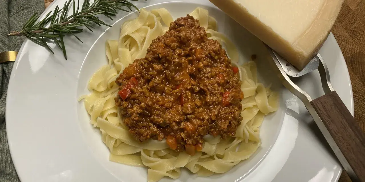 Ein Teller Tagliatelle mit herzhafter Bolognese, garniert mit Rosmarin und Parmesan.