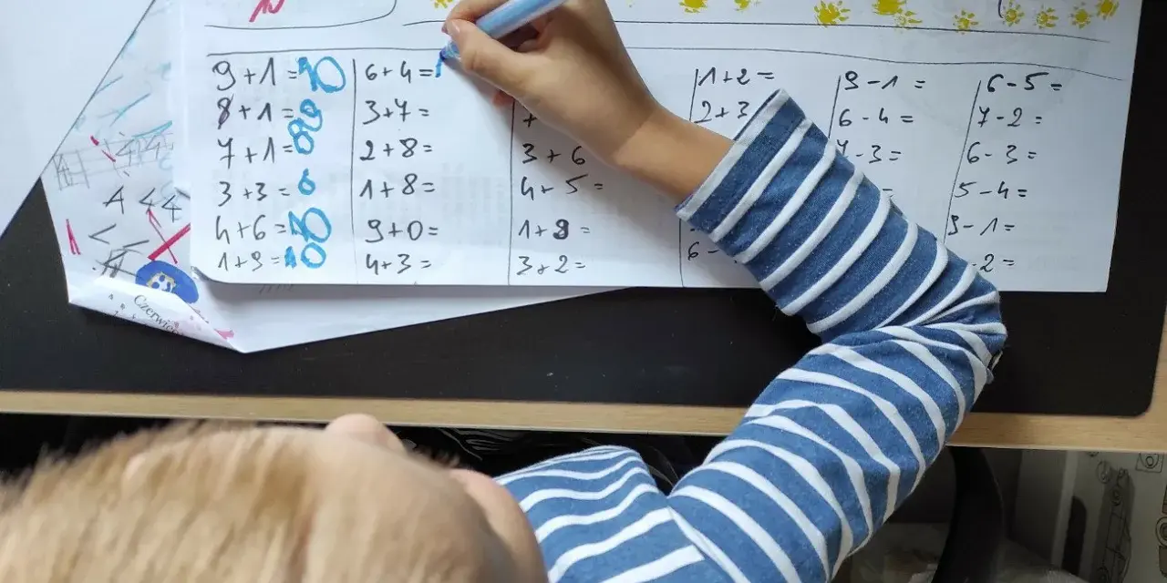 Dziecko rozwiązuje zadania matematyczne. Na kartce widać różne działania, a obok nich cyfry, które mogą stanowić **skalę ocen** lub odpowiedzi.