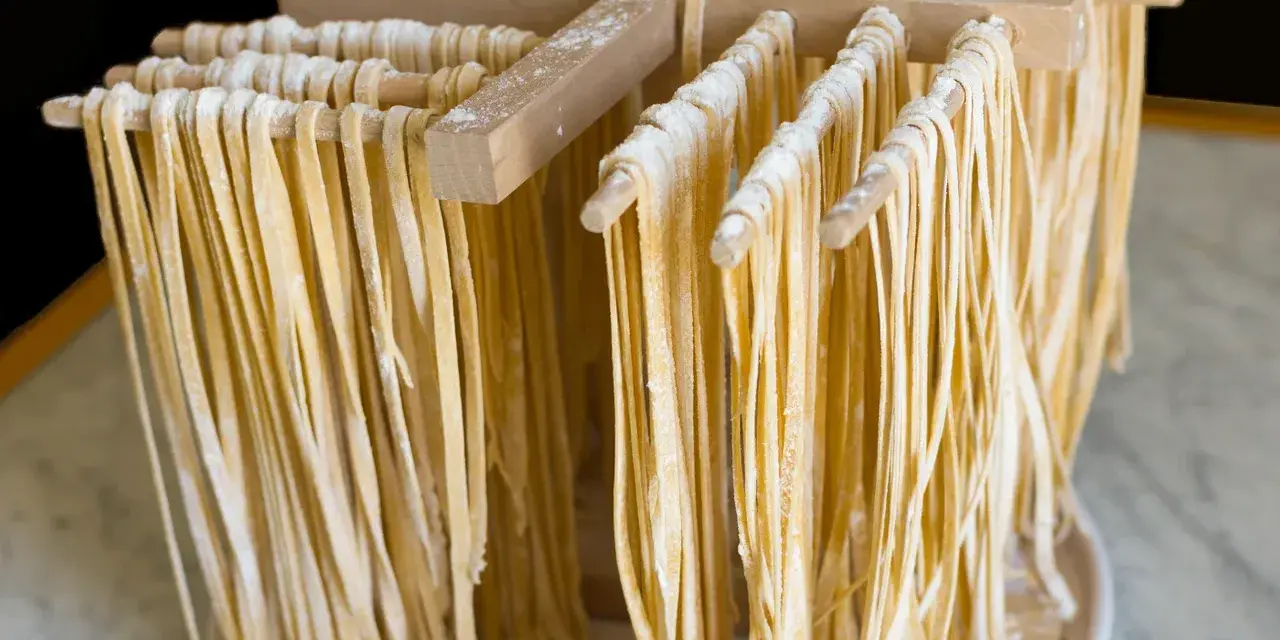 Świeżo przygotowany, domowy makaron tagliatelle suszy się na drewnianym stojaku.