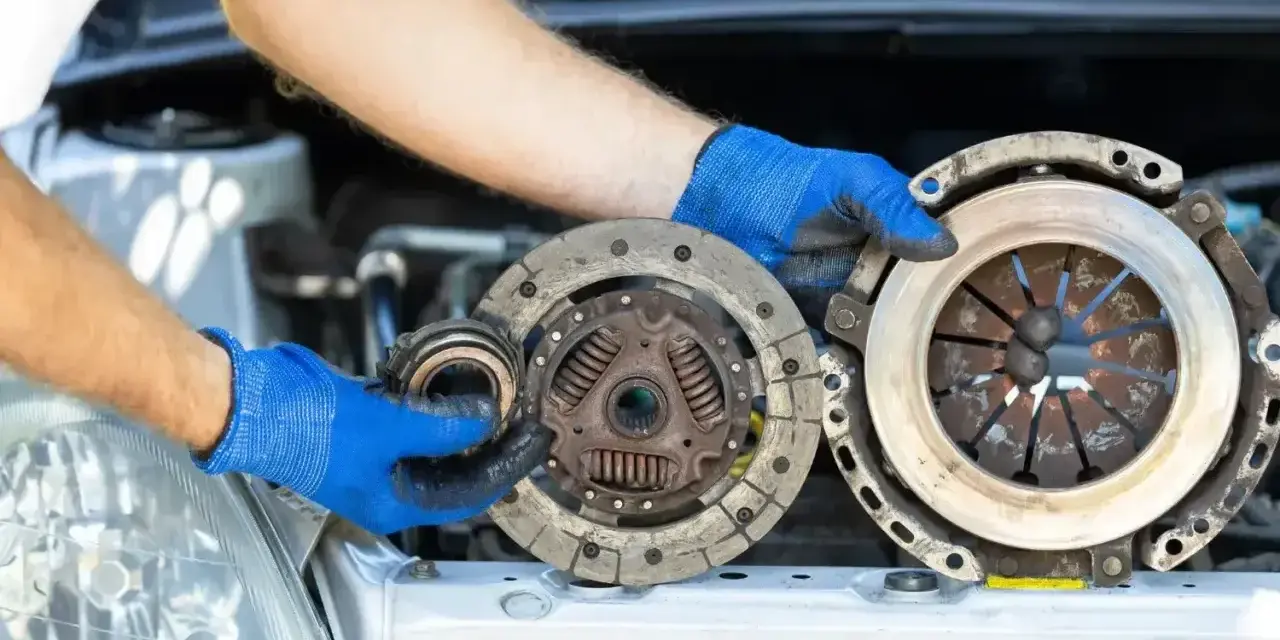 Mechanik w niebieskich rękawiczkach pokazuje zużyte części sprzęgła, które mogą być przyczyną ślizgającego się sprzęgła objawy.