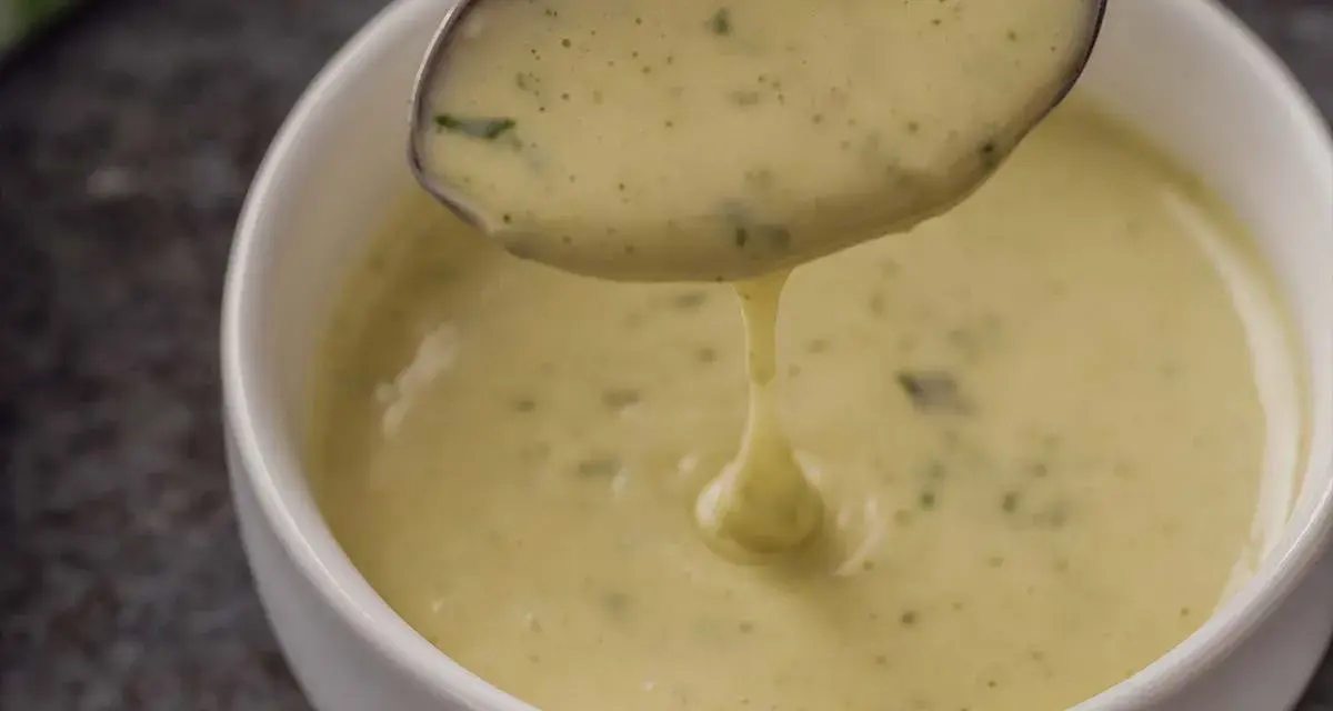 Cremige Sauce Béarnaise tropft von einem Löffel in eine weiße Schüssel.