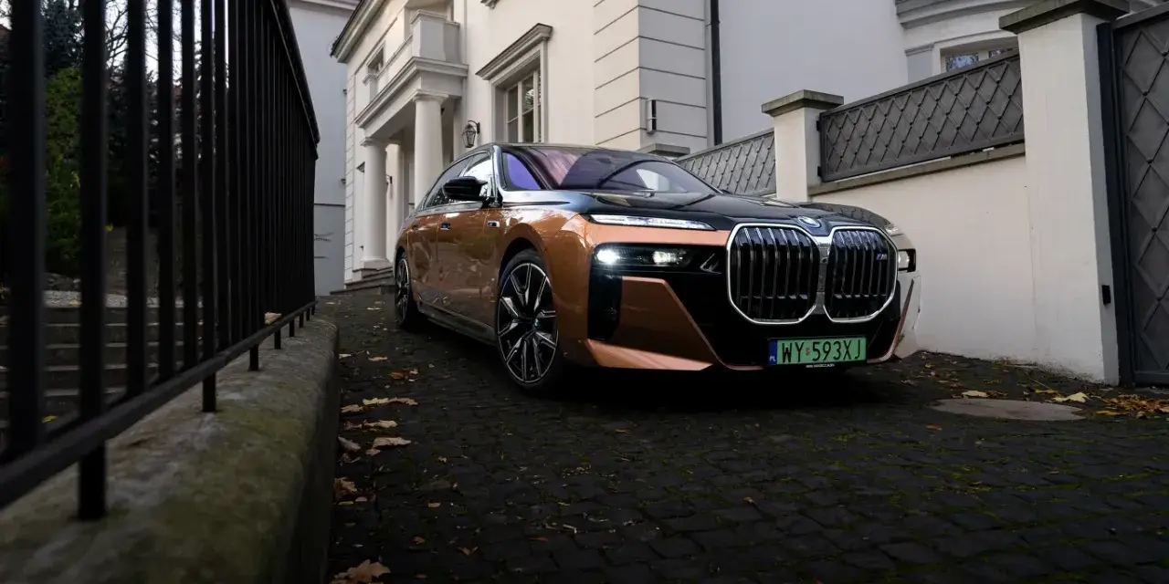 Eleganckie BMW i7 w miedzianym kolorze, zaparkowane przed willą. Ten luksusowy samochód elektryczny oferuje imponujący zasięg, pozwalając na długie podróże.