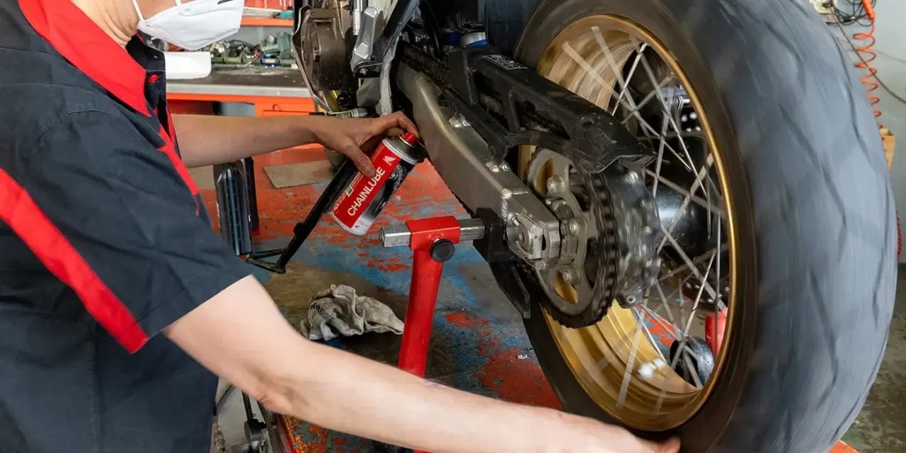 Meccanico lubrifica la catena di una moto. La pulizia catena moto ogni quanti km è fondamentale per la sua durata.
