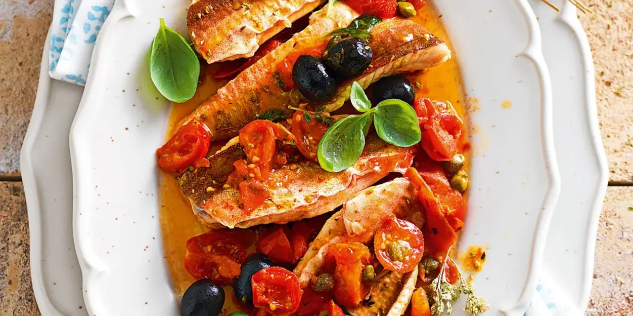 Deliziosa gallinella di mare in umido con pomodorini, olive nere e capperi, guarnita con basilico fresco.