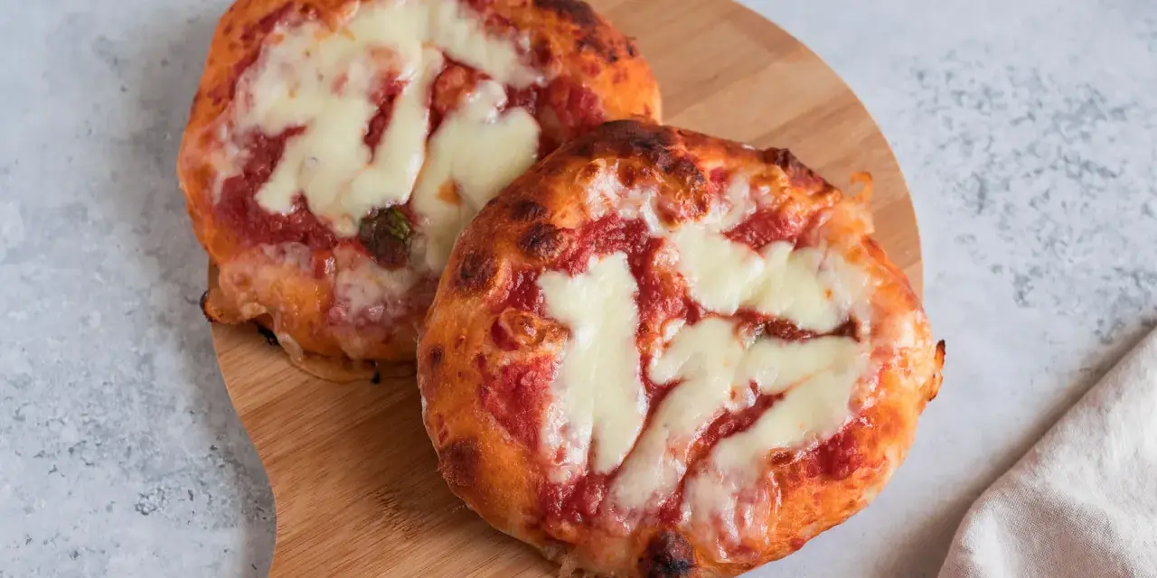 Due pizzette fatte in casa, con pomodoro e mozzarella filante, su un tagliere di legno.