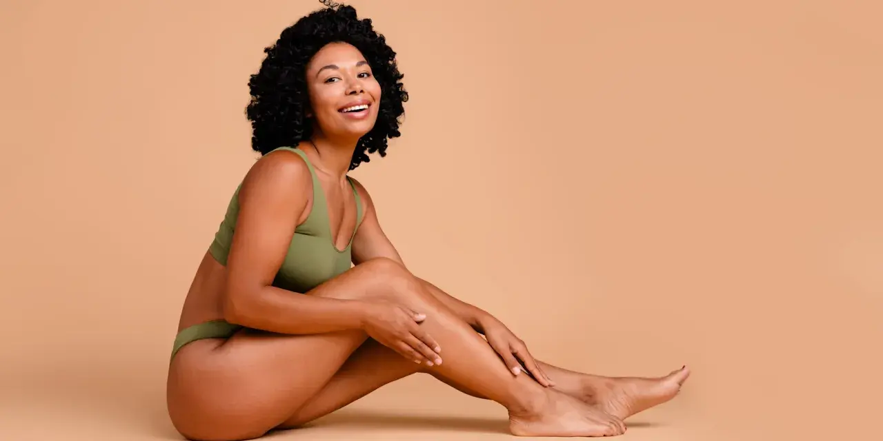 Femme souriante en sous-vêtements verts, caressant sa jambe. Elle partage ses secrets pour comment avoir des pieds doux.