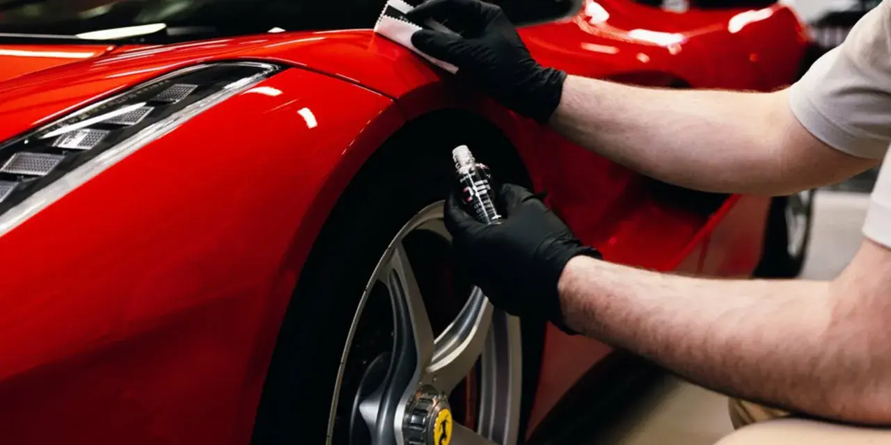 En person med svarta handskar applicerar en skyddande beläggning, troligen **Hydrosilex**, på en röd Ferrari.