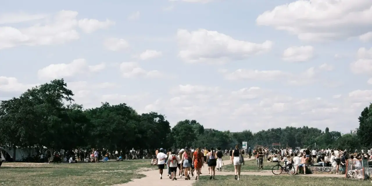 Menschen spazieren an einem sonnigen Pfingstmontag in Berlin durch eine grüne Parklandschaft.