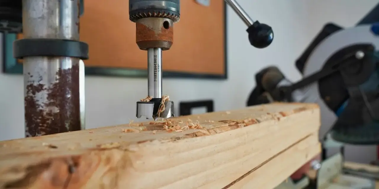 Trapano a colonna che fora un pezzo di legno, creando trucioli. Un esempio pratico di come avvitare una vite nel legno, o meglio, preparare il foro.