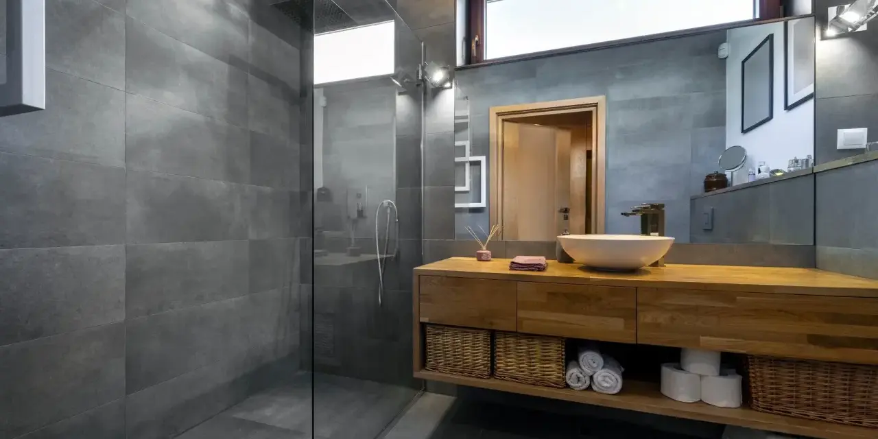 Salle de bain moderne avec douche à l'italienne, carrelage gris, meuble en bois et vasque. Le pose carrelage douche italienne est impeccable.