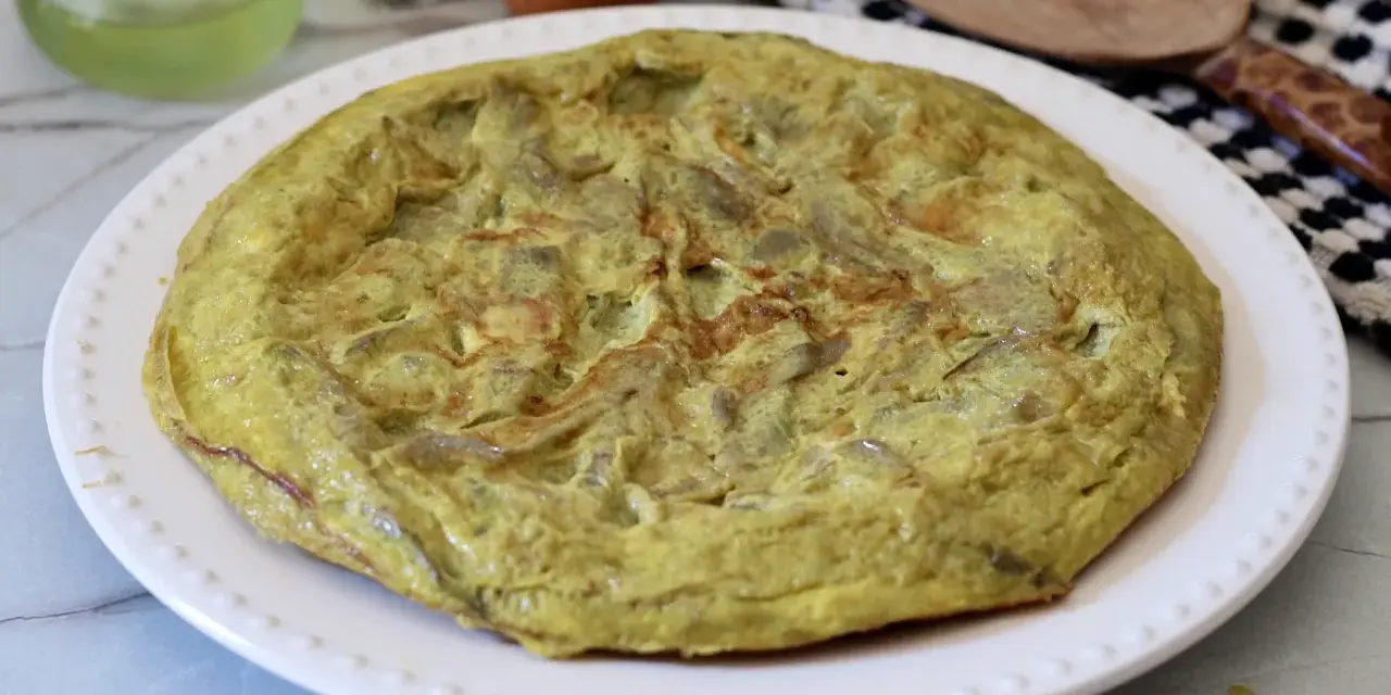 Frittata di carciofi dorata e soffice su un piatto bianco, pronta per essere gustata.