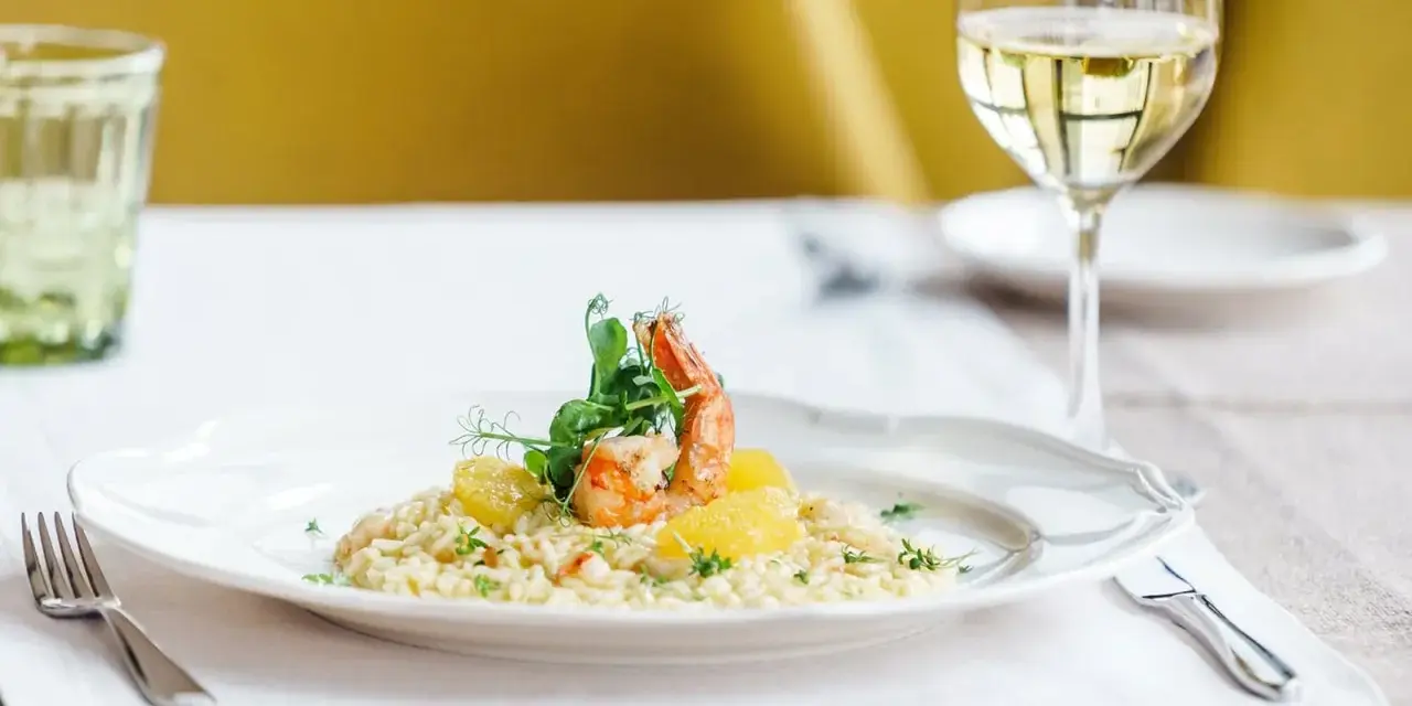 En elegant tallrik med saffransrisotto, toppad med en saftig räka och citrusklyftor. Ett glas vitt vin till saffransrisotto fulländar denna läckra måltid.