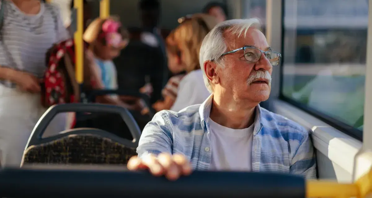 Starszy pan w okularach podróżuje autobusem, ciesząc się darmową komunikacją miejską.
