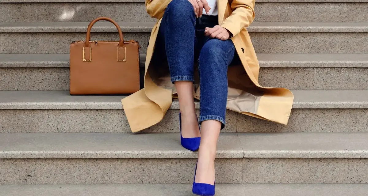 Elegancka stylizacja: beżowy płaszcz, jeansy i buty w kolorze habrowym. Obok torebka w odcieniu karmelu.