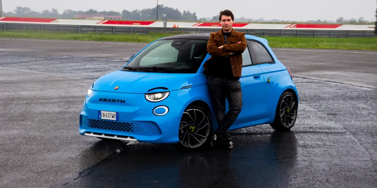 Mężczyzna opiera się o jaskrawo niebieski Abarth 500e na mokrym torze wyścigowym.