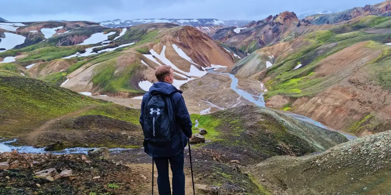Un randonneur admire le paysage coloré de Landmannalaugar, avec ses montagnes aux teintes ocre, vertes et blanches.