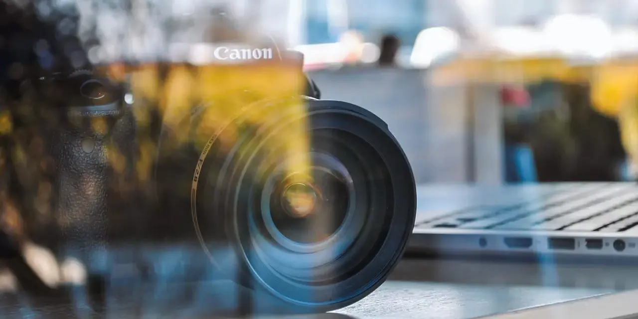 Winieta fotografia: obiektyw Canon na tle laptopa, odbicia tworzą artystyczny efekt.