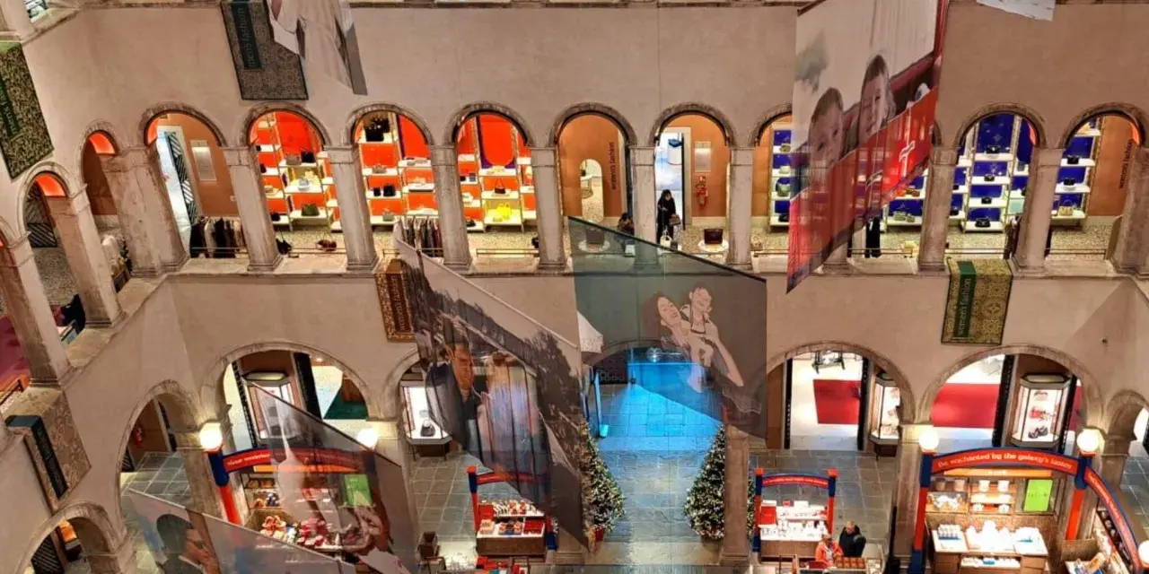 Interno del Fondaco dei Tedeschi, con archi, negozi e grandi stampe appese.