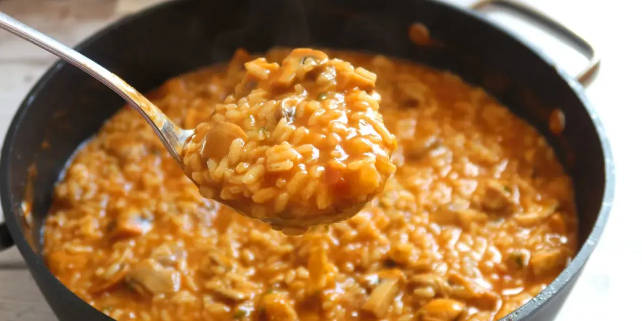 Cuchara llena de cremoso arroz con pollo de la abuela, humeante y con trozos de pollo y champiñones.