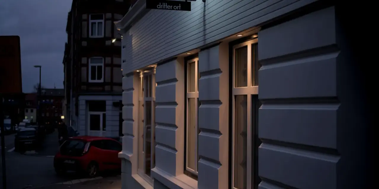 Neon-Schild "fritz-kola" über dem Eingang "dritter ort kiel". Ein rotes Auto parkt auf der Straße.