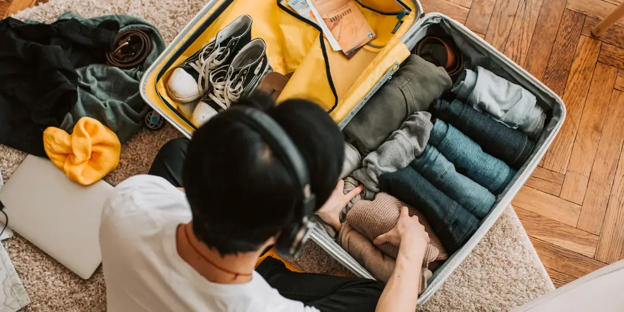 Preparazione per il mare: una valigia piena di vestiti piegati, scarpe, una felpa gialla e un laptop. Ecco cosa portare in vacanza al mare!