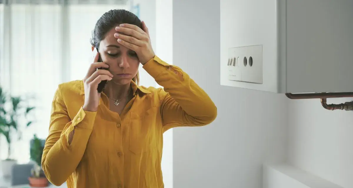 Donna preoccupata al telefono vicino allo scaldabagno, cerca consigli su come evitare il calcare.