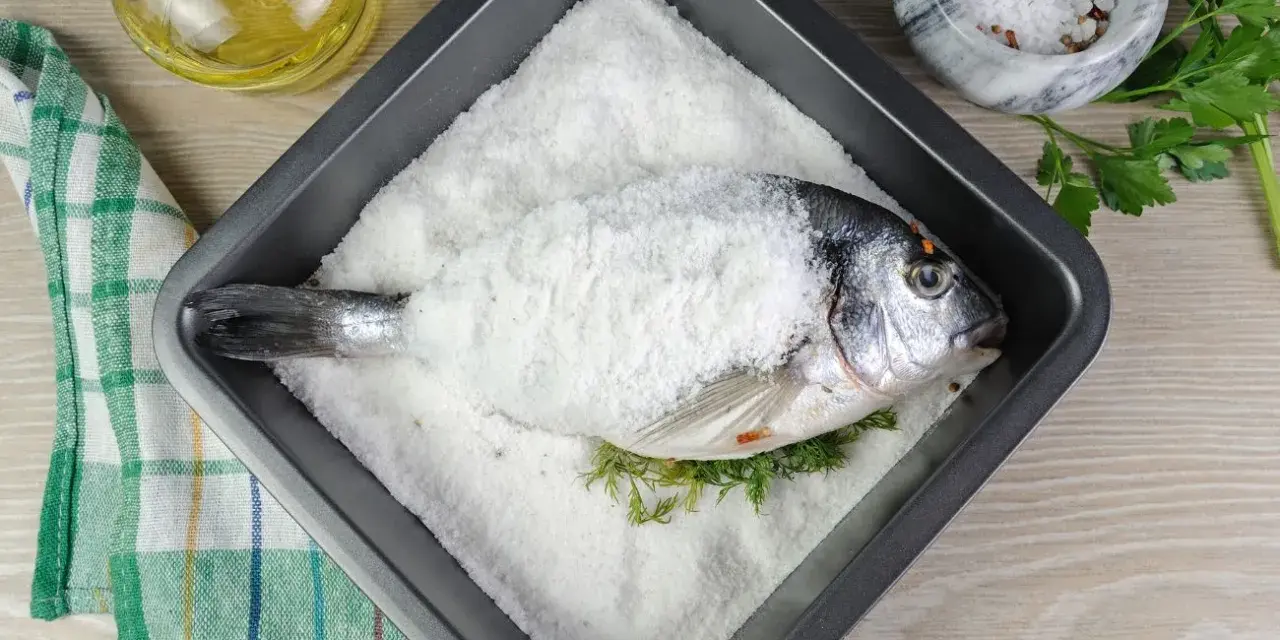 Dorada a la sal lista para hornear, con hierbas frescas y aceite de oliva al lado.