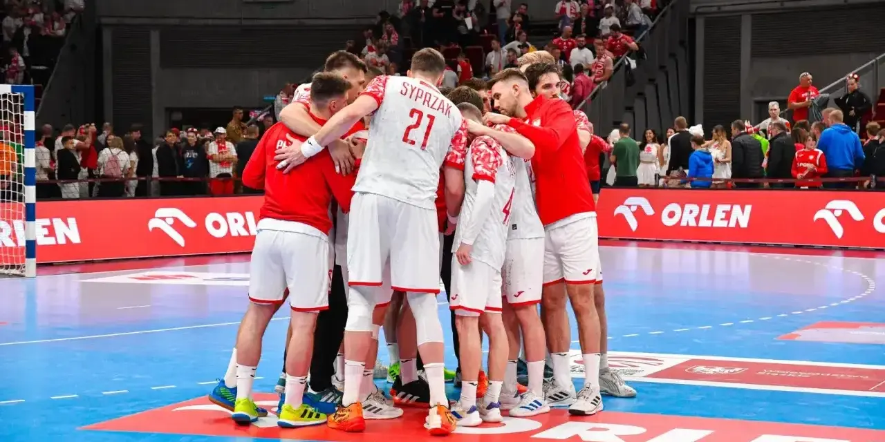 Drużyna piłkarzy ręcznych w białych strojach z czerwonymi elementami tworzy zgraną grupę na boisku.