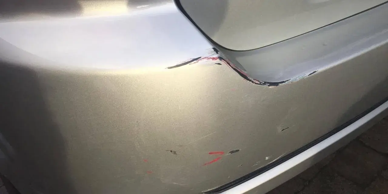 Skadad bakre stötfångare på en silverfärgad bil. Repor och skrapmärken syns tydligt. Undrar du över laga lackskada pris?