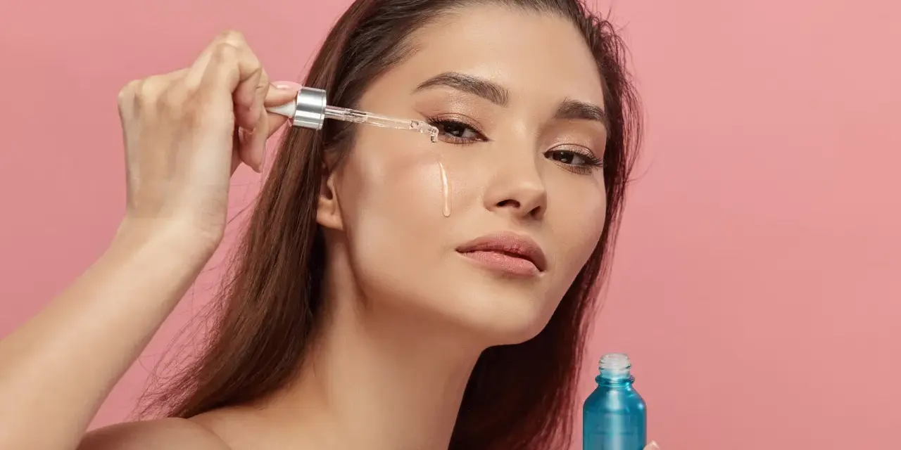 Kobieta aplikuje serum z retinyl palmitate na skórę pod okiem. Błękitna buteleczka kosmetyku w dłoni.