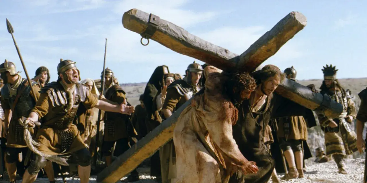 Scena z filmów chrześcijańskich: Jezus dźwigający krzyż, otoczony przez żołnierzy.
