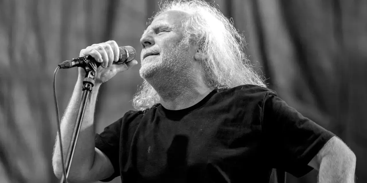Roman Kostrzewski, wokalista zespołu Kat, śpiewa z pasją do mikrofonu. Długie, siwe włosy artysty opadają na ramiona.