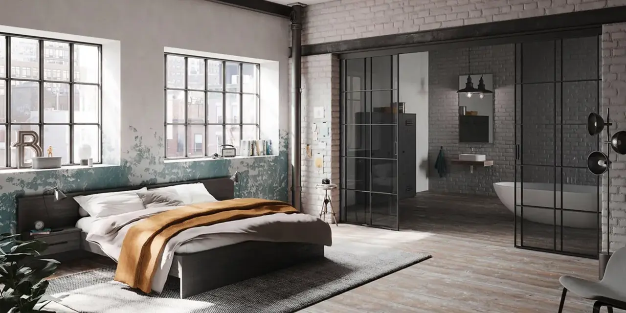 Ein gemütliches **Bett unter Fenster** mit industriellem Charme. Daneben ein offener Badbereich mit Wanne.