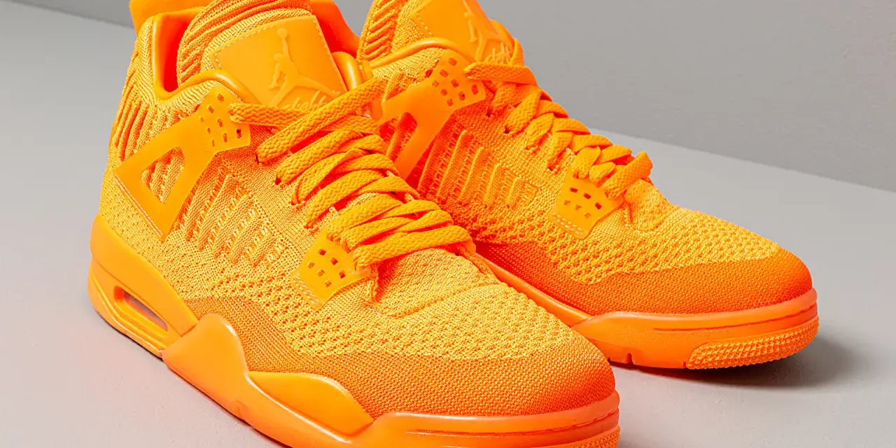 Un paio di scarpe Jordan 4 arancioni brillanti, con tomaia in maglia e dettagli iconici.