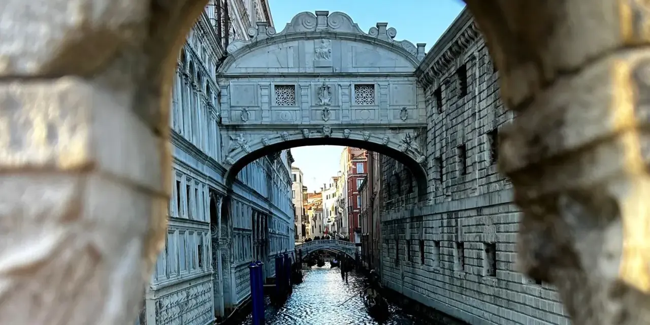 Il Ponte dei Sospiri a Venezia, visto da un'arcata, con gondole sull'acqua e un cielo azzurro.