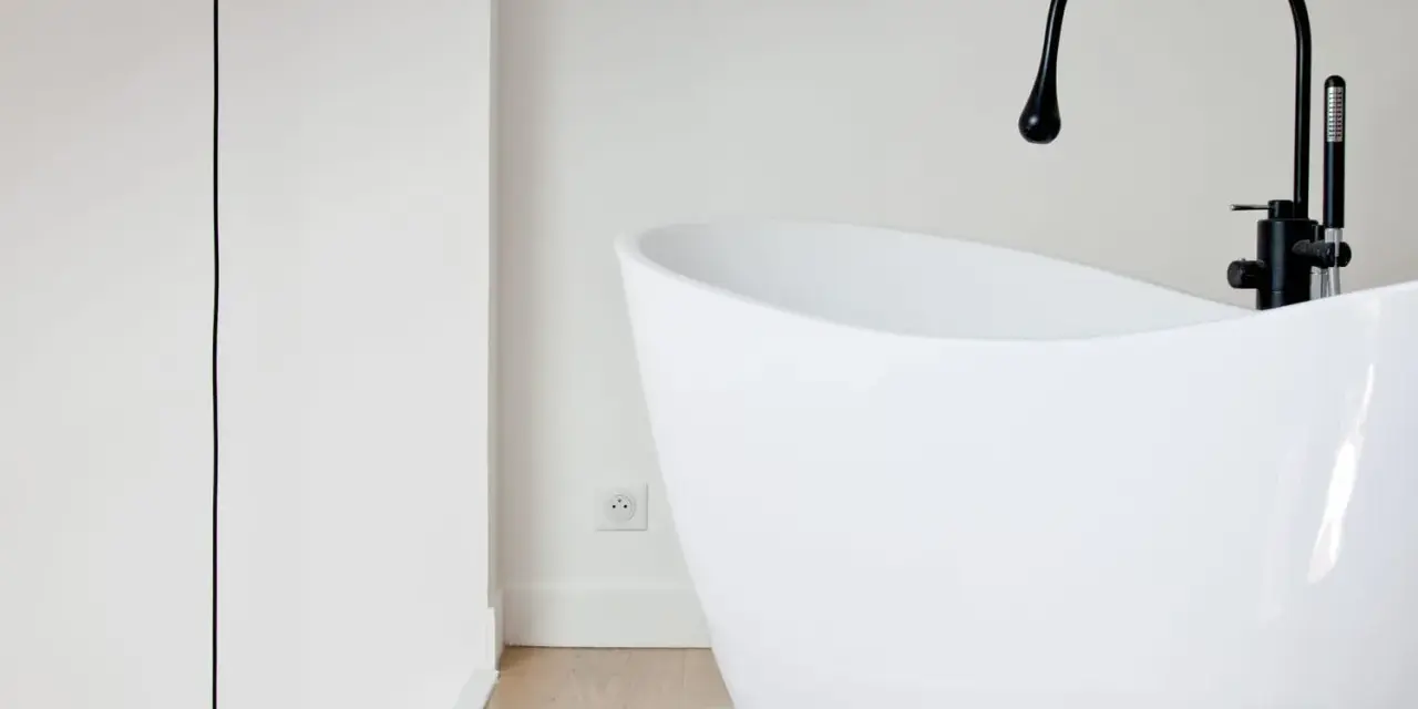 Baignoire îlot blanche au design moderne, avec robinetterie noire. Sa forme suggère une largeur baignoire standard, idéale pour un confort optimal.