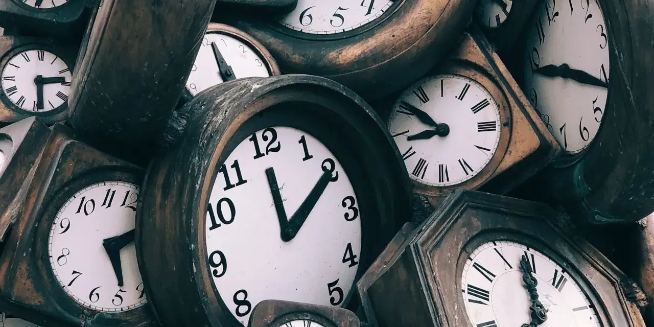 Stos starych zegarów, niektóre z rzymskimi cyframi, inne z arabskimi.