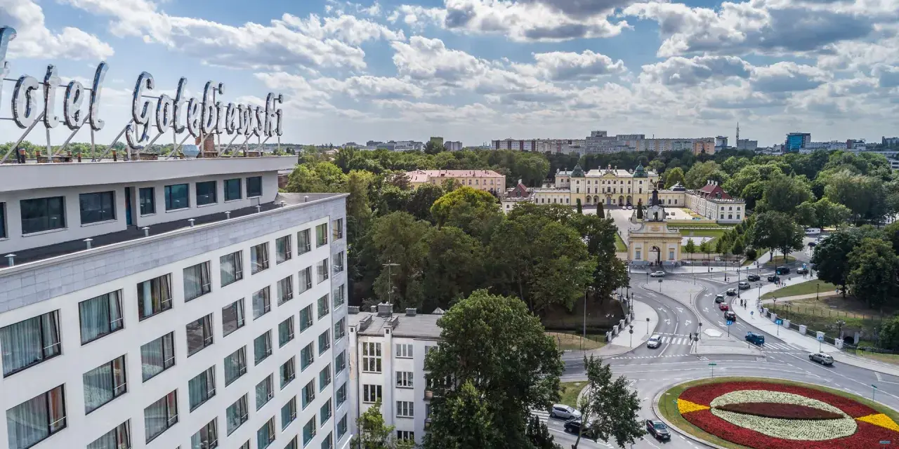 Widok na hotel Gołębiewski w Łodzi z charakterystycznym neonem. W tle rozciąga się miasto z zielenią i budynkami.