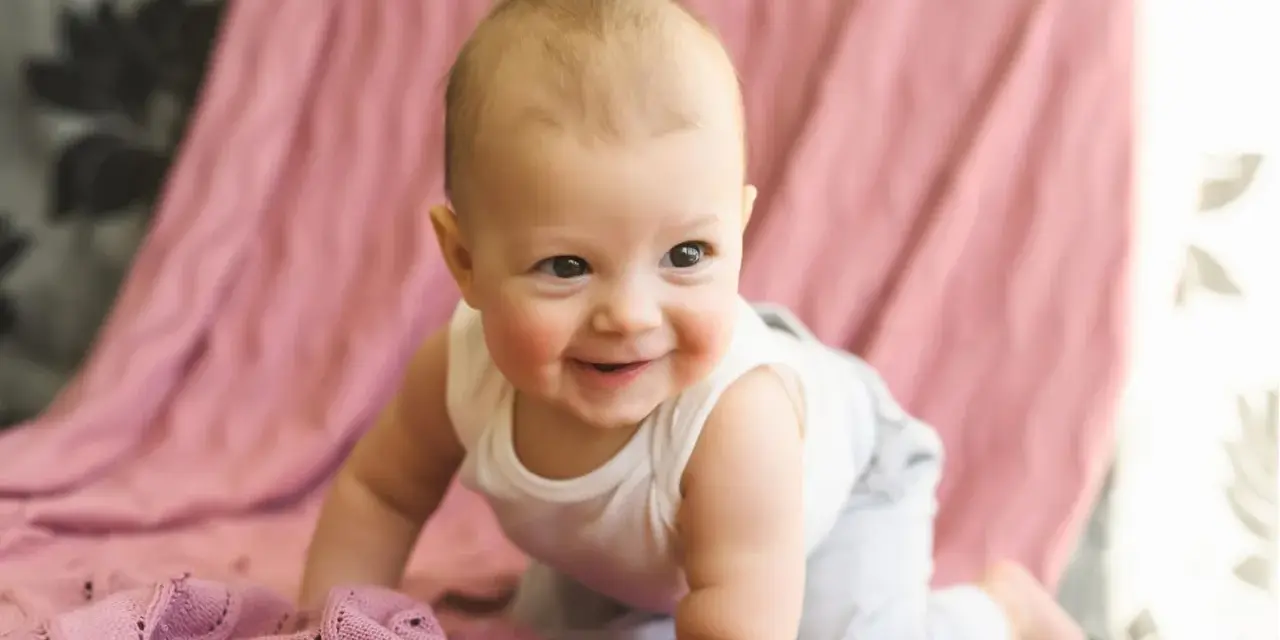 Ein lächelndes Baby krabbelt auf einer rosafarbenen Decke. Es ist etwa 26 Wochen alt und erlebt gerade einen Entwicklungsschub.