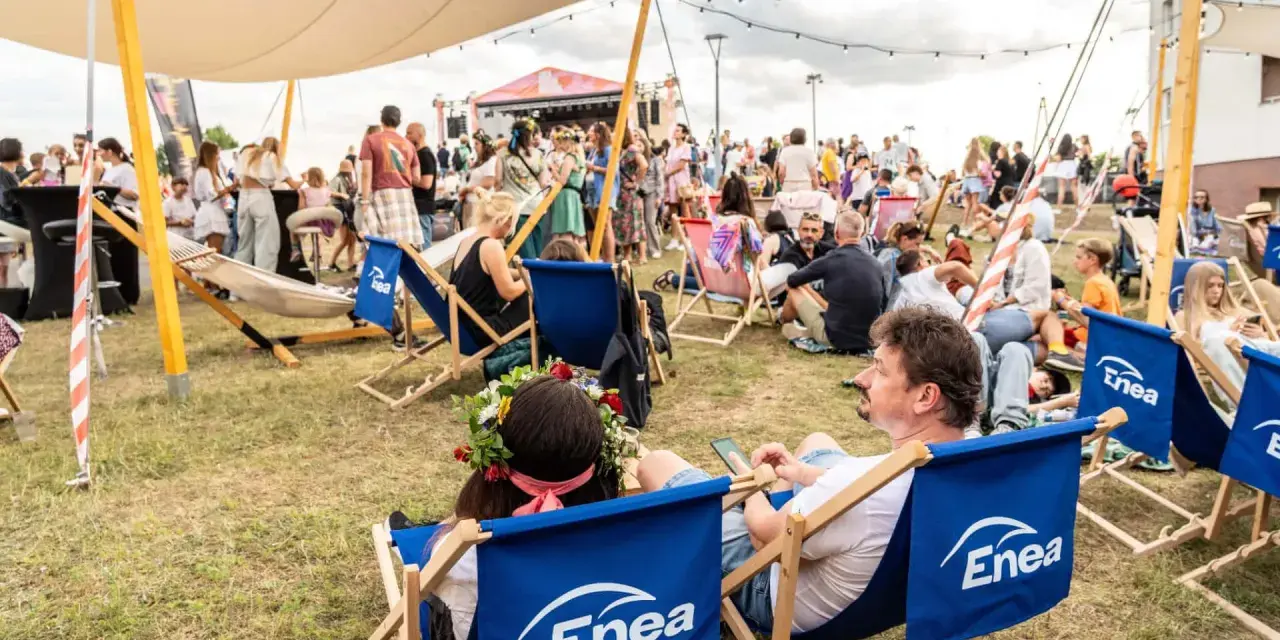 Ludzie odpoczywają na leżakach z logo Enea podczas festiwalu. W tle scena i tłum.