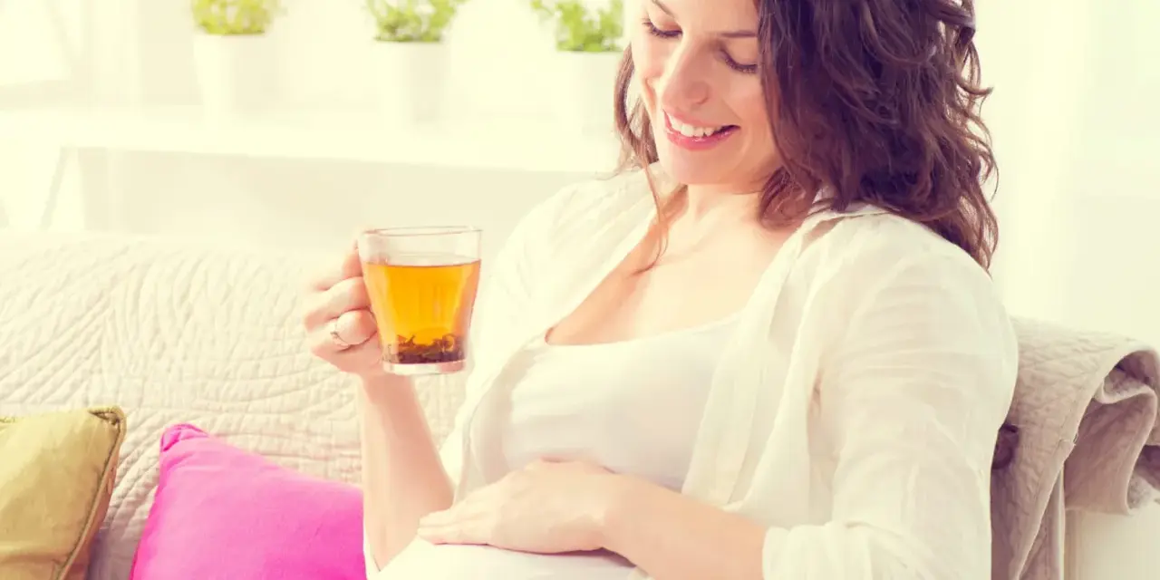 Femme enceinte souriante tenant une tasse d'infusion de thym, posant sa main sur son ventre.