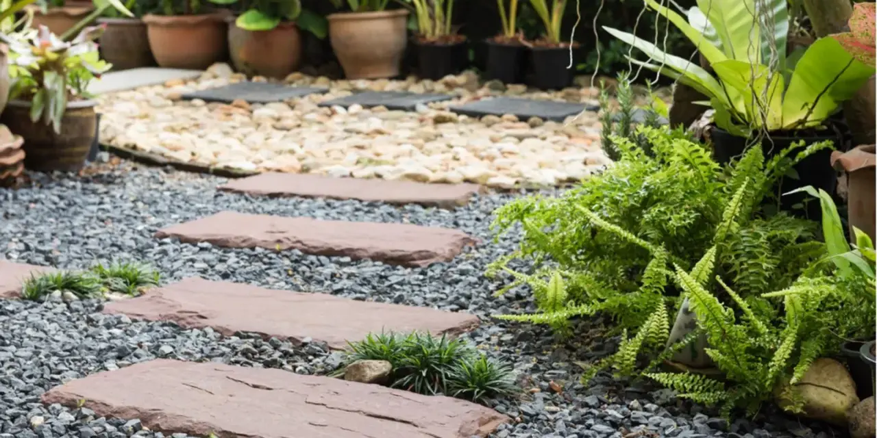 Schrittplatten führen durch einen Kiesgarten. Ein Steingarten anlegen wird hier mit Farnen und Gräsern umgesetzt.