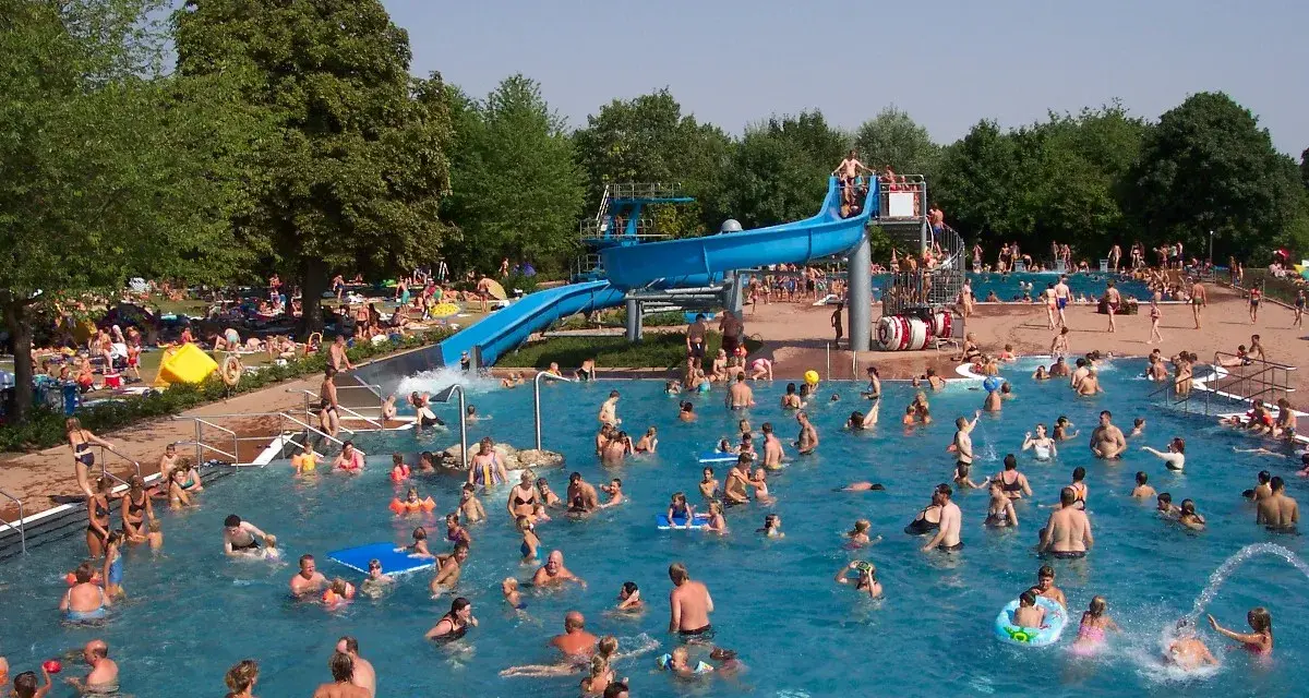 Ein belebtes Freibad in Goslar mit vielen Menschen, die im Wasser planschen und die blaue Wasserrutsche genießen.