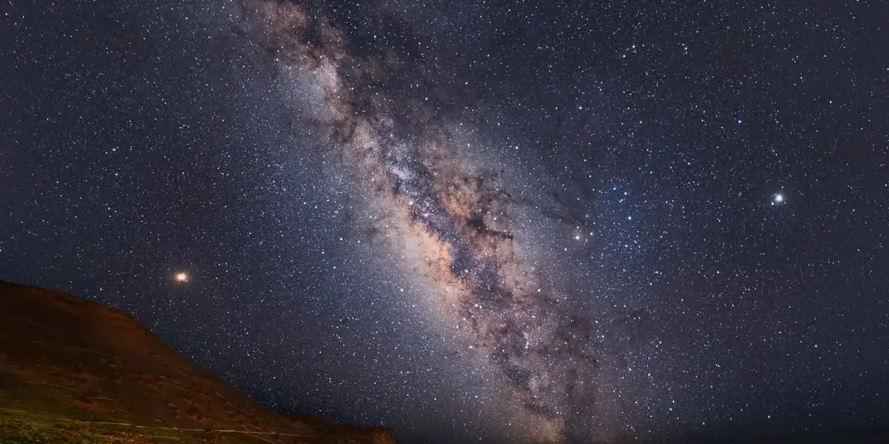 Paisaje nocturno en una reserva starlight, con la Vía Láctea cruzando el cielo estrellado sobre una colina y vegetación.