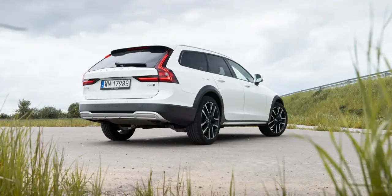 Białe Volvo Cross Country na tle pochmurnego nieba i zielonych wzgórz.