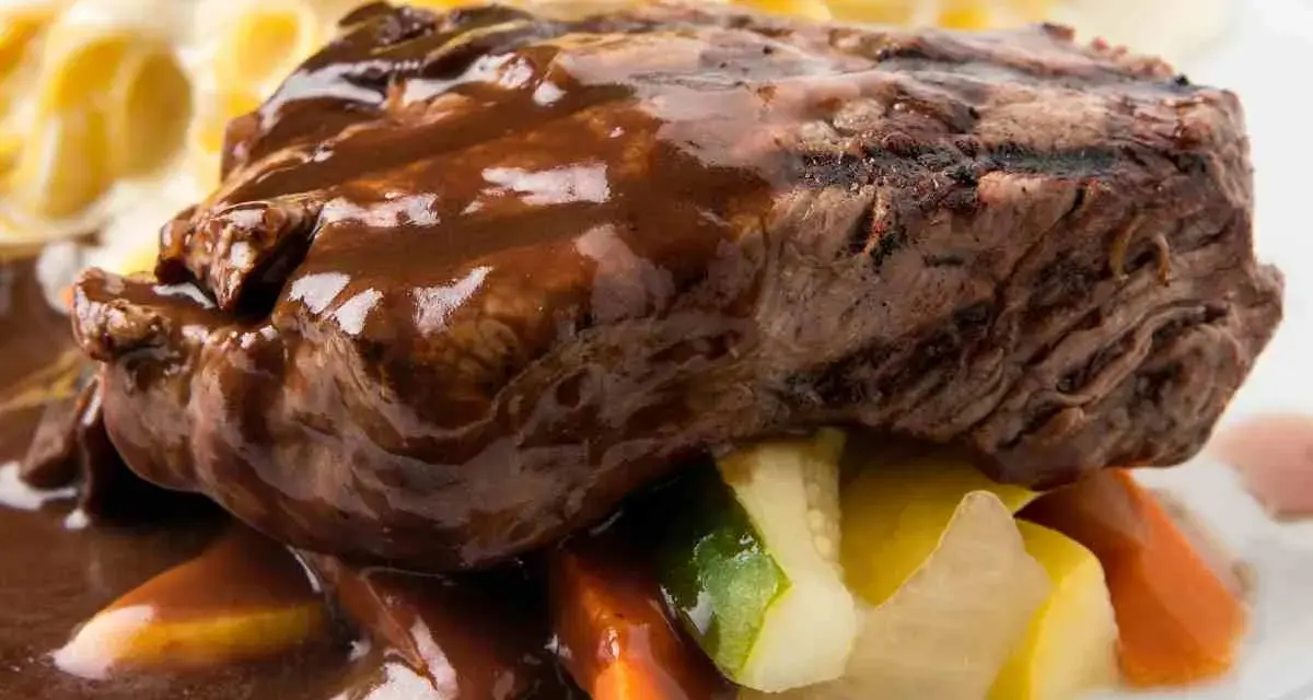 Succulento brasato di manzo nappato con salsa scura, servito su verdure miste e accompagnato da pasta.